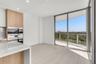 Floor-to-ceiling sliding glass doors opening to a private balcony, wood-finish cabinetry, built-in stainless steel wall ovens, and stone-surfaced isla