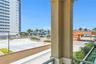 Covered balcony with a textured stucco support pillar, overlooking an exterior surface parking area, landscaped masonry planters, and a coastal landsc