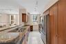 Kitchen featuring wood-veneer cabinetry, stone countertops, stainless steel appliances, dual-basin under-mount sink, and large-format tile flooring