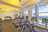 Fitness center featuring recessed tray ceiling lighting, floor-to-ceiling arched windows, and ocean backdrop