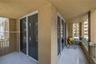 Covered balcony featuring white tiled flooring, stucco walls, dual sliding glass door access, and green metal railings