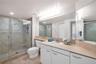 Full-width vanity with a neutral solid-surface countertop and recessed basin, glass-enclosed shower with tile surround, and expansive wall-to-wall mir
