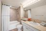 Bathroom featuring a recessed tub with a tile surround, a built-in vanity with a solid-surface countertop, an integrated oval sink, and a full-width w