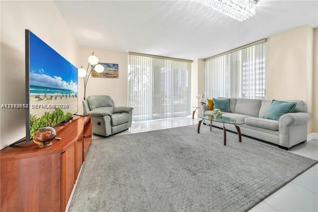 Open-concept living space featuring high-gloss tile flooring, floor-to-ceiling vertical blinds, and a modern crystal flush-mount light fixture