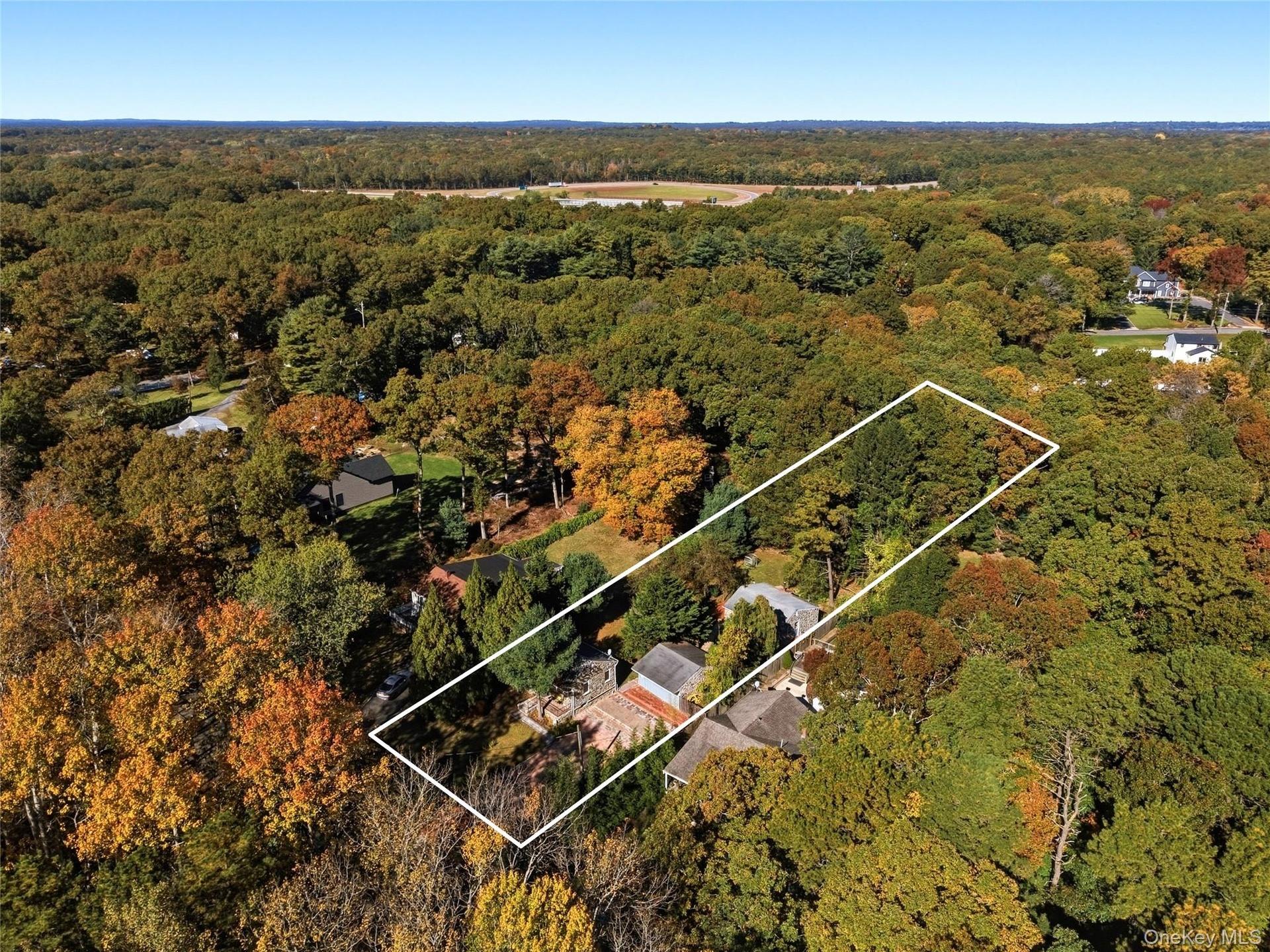 Aerial perspective of a multi-structure property featuring mature woodland surroundings, a paved driveway, and stone hardscaping