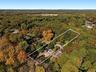 Aerial perspective of a multi-structure property featuring mature woodland surroundings, a paved driveway, and stone hardscaping
