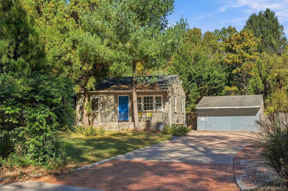 Stone exterior residence featuring a front entry with metal railing, a detached garage, and a brick-paved driveway surrounded by mature trees
