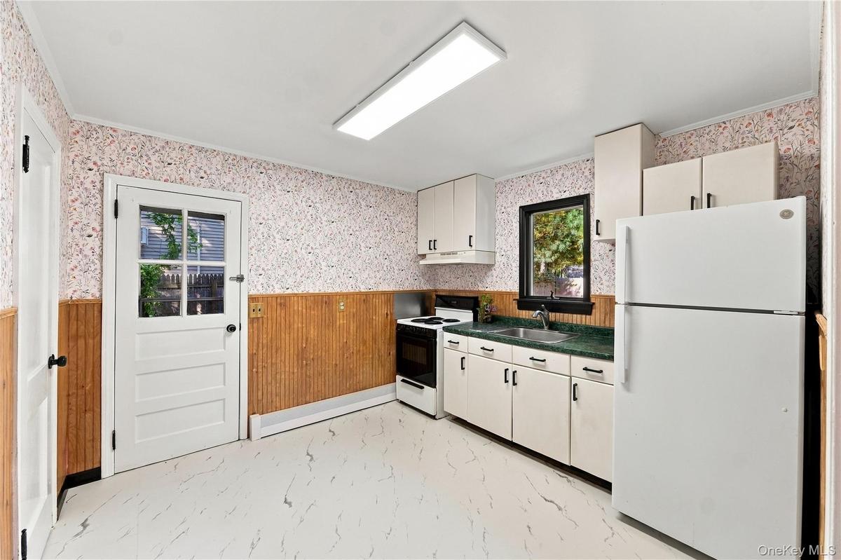 Kitchen featuring white cabinetry, solid-surface countertops, paneled wainscoting, and direct exterior access