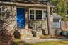 First Cottage. Exterior facade featuring natural stone masonry, a vibrant blue entry door, and  front porch enclosed by decorative iron railing
