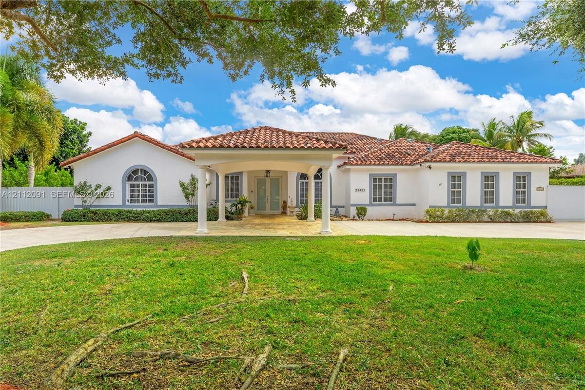 Stucco exterior featuring a covered porte-cochère, red tile roofing, arched windows, and a paved circular driveway