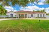 Stucco exterior featuring a covered porte-cochère, red tile roofing, arched windows, and a paved circular driveway