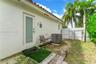 Exterior side yard featuring white stucco siding, a glass-panel door, terracotta roof tiles, a white vinyl privacy fence, and mature palm trees