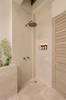 Shower featuring a wall-mounted rain shower head, natural stone wall cladding, built-in recessed wall niche, and stone tile flooring, paired with a lo
