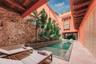 Open-air courtyard featuring a swimming pool, exposed stone walls, wooden beam ceilings, integrated raised planter, and balcony with wooden shutters