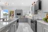 Kitchen featuring gray Shaker-style cabinetry, white solid-surface countertops, stone-tile backsplash, stainless steel appliances, and large-format po