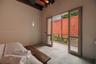 Vaulted ceiling with exposed wood beams, light-toned stone flooring, and full-length glass paneled doors opening to a private exterior balcony with a 