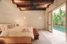 Exposed timber ceiling beams, ceiling fan, wall-mounted light fixtures, stone flooring, and glass door opening to a private pool