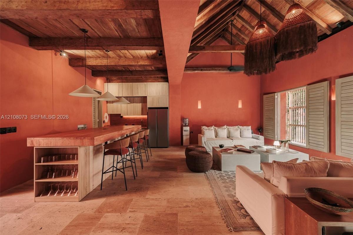 Open-concept living space featuring vaulted ceilings with exposed wood beams, stone tile flooring, a built-in kitchen island with integrated shelving,