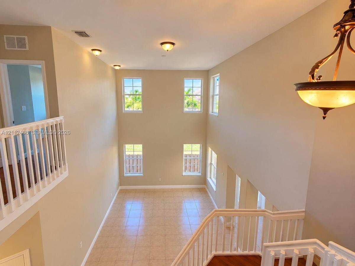 Double-height ceiling, large windows with natural light, tile flooring, and white spindle railings