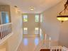Double-height ceiling, large windows with natural light, tile flooring, and white spindle railings