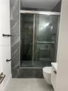Walk-in shower featuring floor-to-ceiling large-format tile, sliding glass door, wall-mounted matte black hardware, and an elongated toilet