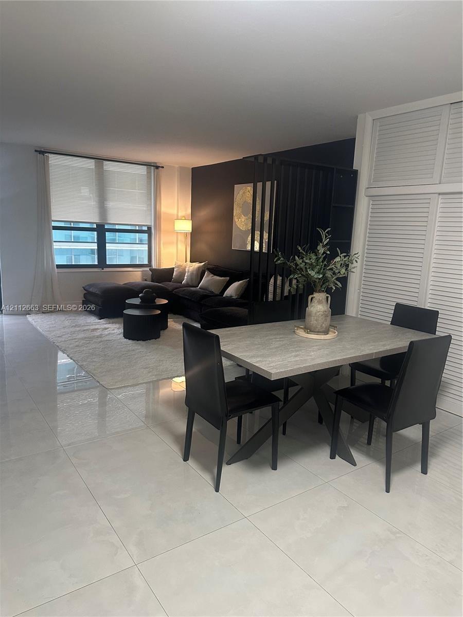 Open-concept interior featuring large-format tile flooring, a black-painted accent wall, built-in louvered-style closet doors, and expansive windows