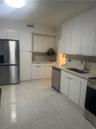Kitchen featuring flat-panel white cabinetry, stainless steel appliances, light-toned solid surface countertops, and large-format tile flooring