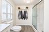 Bathroom featuring wood-finish flooring, a walk-in shower with a glass enclosure and built-in bench, stone-patterned vanity countertop, and wall-mount