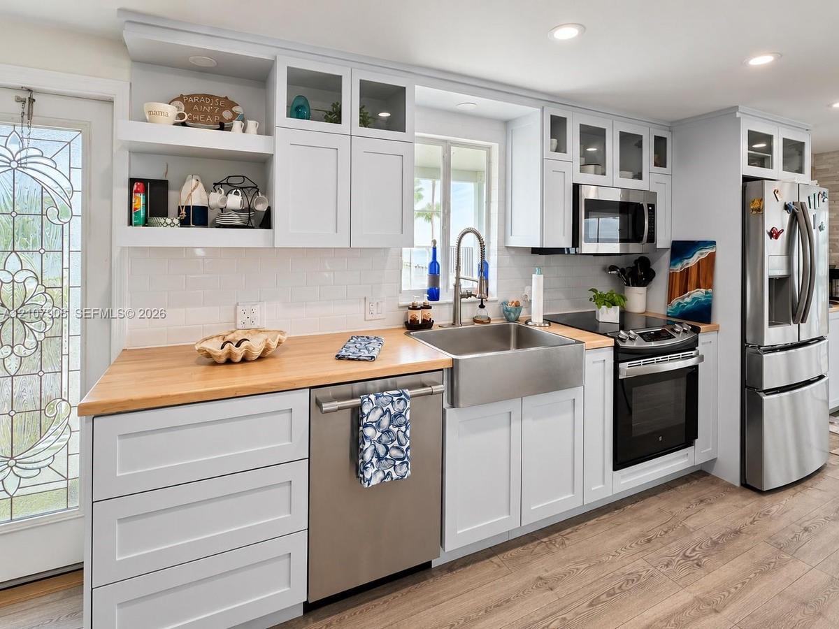 Kitchen featuring white shaker-style cabinetry, wood-finish countertops, stainless steel farmhouse sink, glass-front upper cabinet doors, and wood-fin