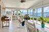 Enclosed sunroom featuring floor-to-ceiling screen panels, white tile flooring, natural stone-accent wall, and a ceiling fan