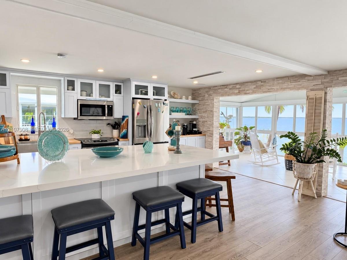 Kitchen featuring a white quartz island countertop, stainless steel appliances, white cabinetry with glass-front uppers, stacked stone accent wall, an