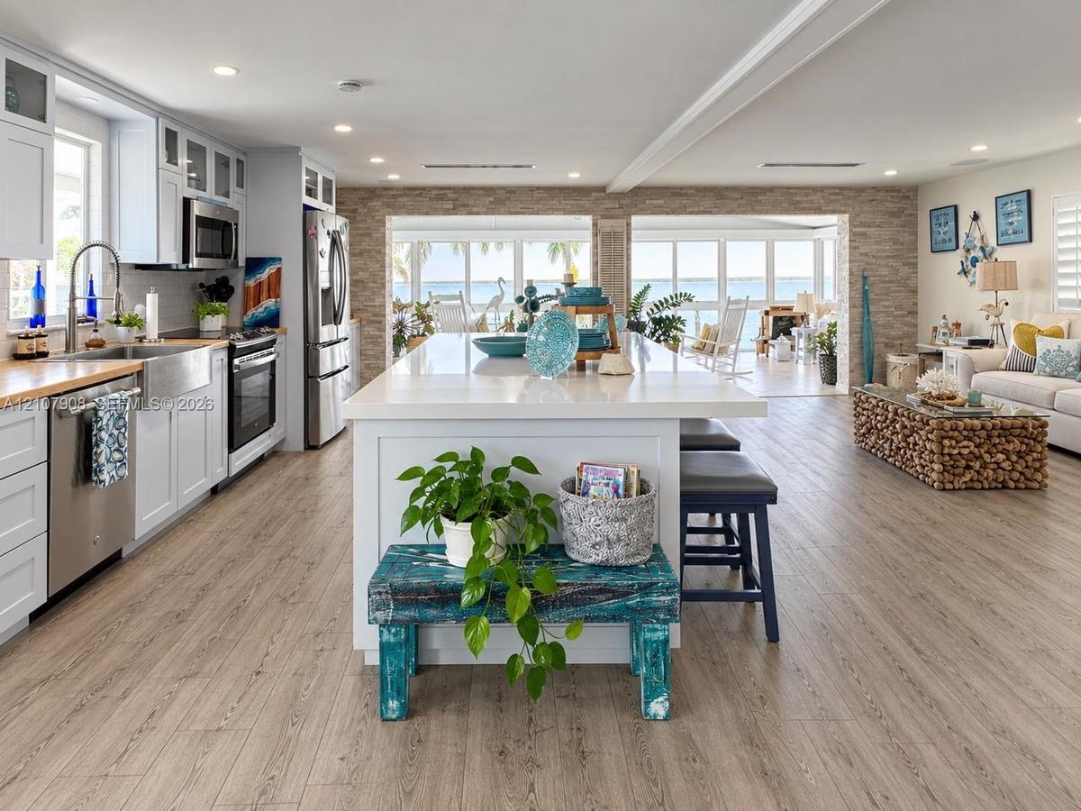 Kitchen featuring white shaker-style cabinetry, stainless steel appliances, a farmhouse sink, a central island with a solid surface countertop, and wo