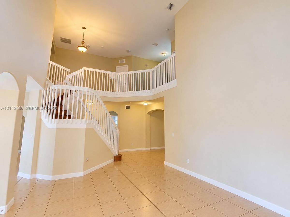 Two-story foyer featuring high ceilings, tile flooring, an open staircase with white balusters, arched entryways, and pendant lighting