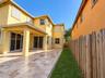 Stucco exterior featuring a covered patio with tile flooring, recessed outdoor lighting, dual sliding glass doors, and a wood-slat perimeter fence