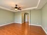 Room featuring wood-finish flooring, a tray ceiling, an arched entryway, and an attached ceiling fan with a light fixture