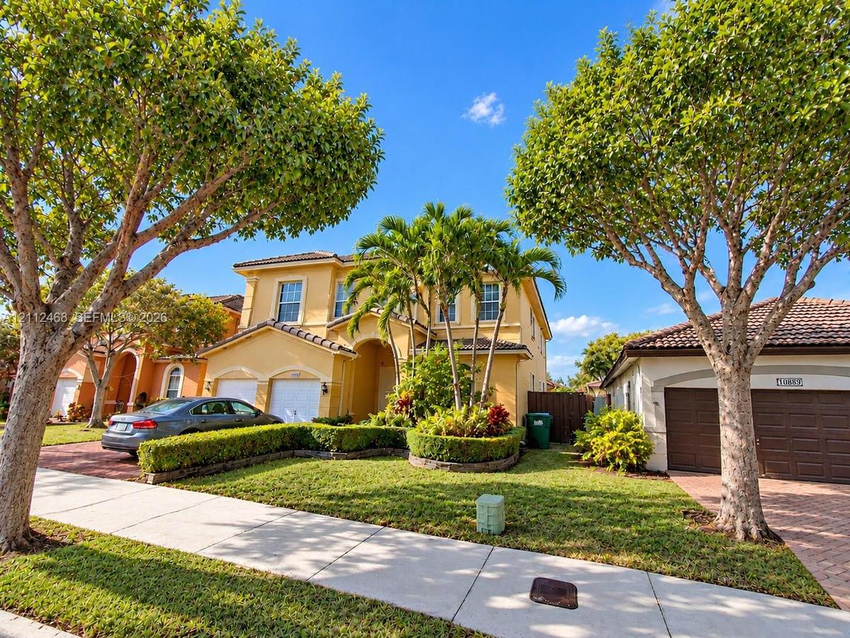 Two-story stucco exterior featuring a multi-gabled tile roof, arched entryway, and integrated two-car garage with brick-paver driveway