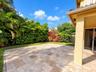 Covered patio featuring stone-tiled flooring, landscaped lawn, mature privacy hedges, and flowering shrubs
