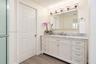 White shaker-style cabinetry vanity with a stone countertop, undermount sink, multi-bulb overhead lighting, and wood-finish flooring
