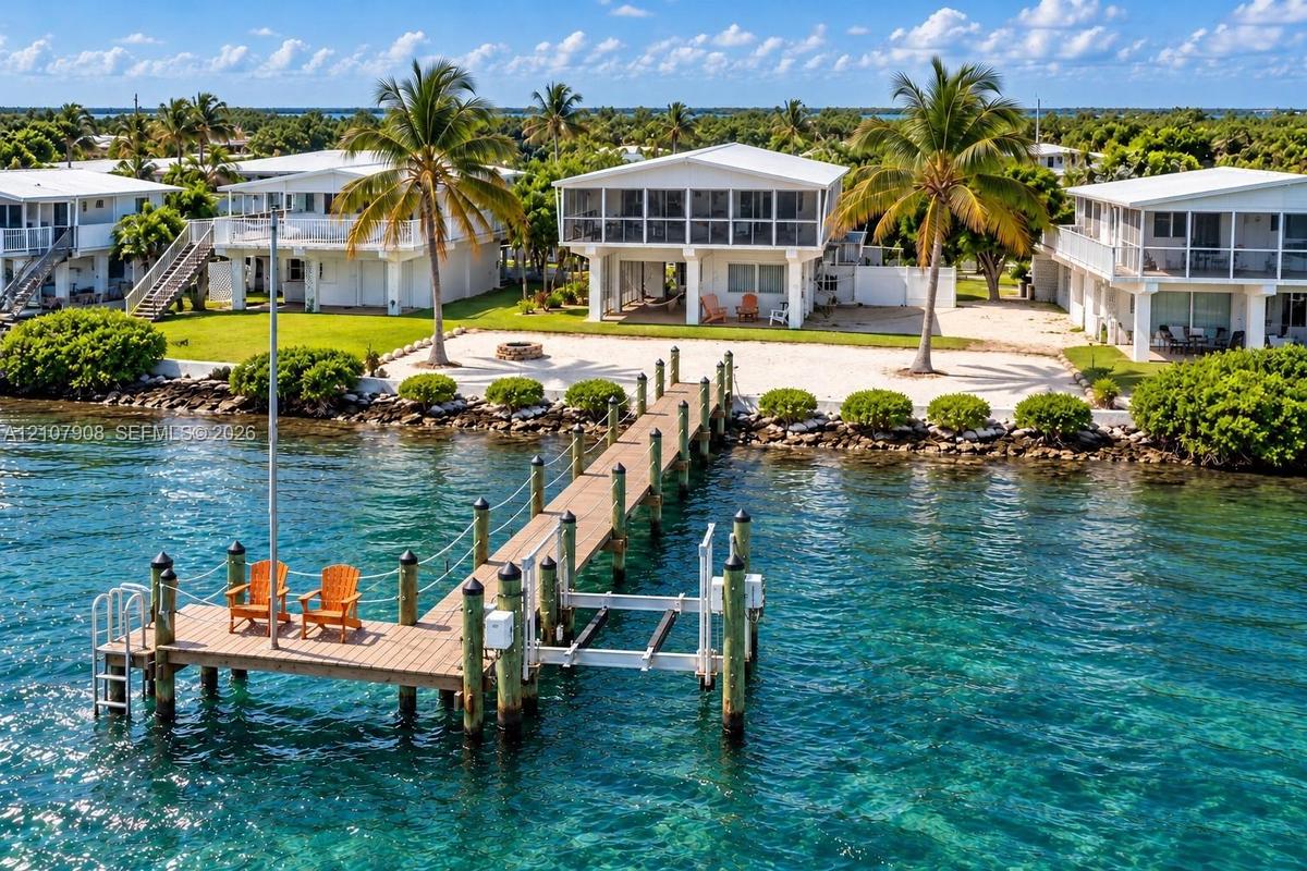 Waterfront property featuring a private wooden pier, boat lift, rock-lined shoreline, and elevated screened lanai