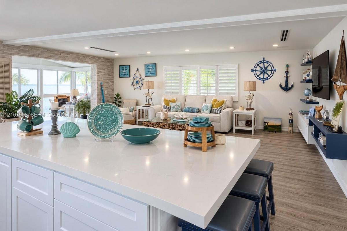 Oversized kitchen island with quartz countertop, light wood-finish flooring, stone-textured accent wall, recessed lighting, and white plantation shutt