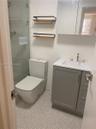 Bathroom featuring a gray vanity cabinet with an integrated white sink, wall-mounted mirrored medicine cabinet, glass-enclosed shower, dual tiered woo