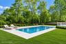 Rectangular inground pool with stone coping, expansive manicured lawn, perimeter fencing, and mature trees