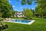 Expansive backyard featuring a rectangular in-ground pool, stone pool deck, meticulously manicured lawn, and mature trees