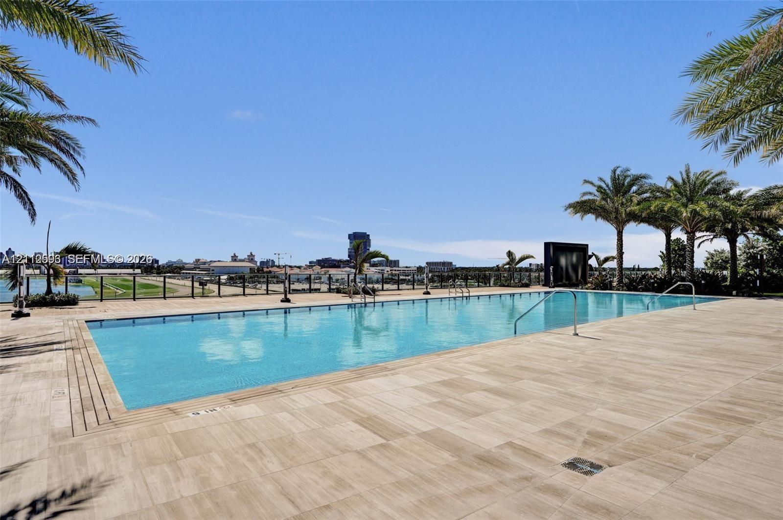 Rectangular swimming pool featuring a tile deck, metal perimeter railing, and palm tree landscaping