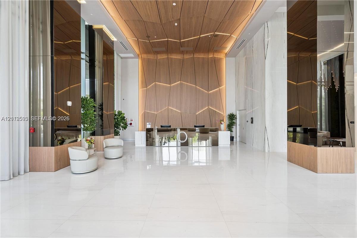 Grand lobby featuring large-format tile flooring, reflective mirror-clad columns, and a geometric wood-paneled accent wall with integrated linear ligh