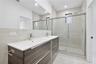 Floating double vanity with a white countertop and dual chrome faucets, complemented by a large wall-to-wall mirror, walk-in shower with sliding glass