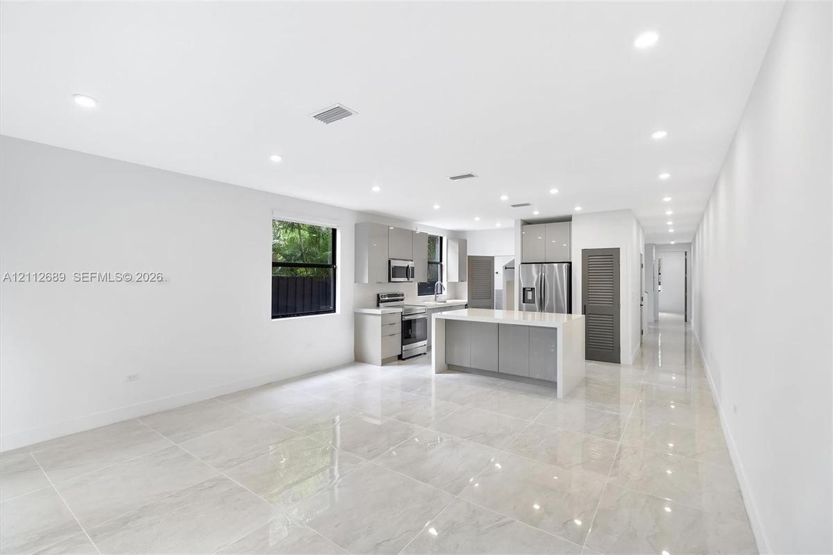 Kitchen featuring high-gloss cabinetry, stone-finish countertops, stainless steel appliances, a central island, and large-format porcelain tile floori