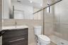 Wall-mounted vanity with a rectangular sink, full-width mirror, walk-in shower with sliding glass doors, and neutral large-format tile wall cladding