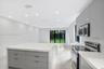 Modern kitchen featuring high-gloss cabinetry, stone-surface waterfall island, stainless steel appliances, recessed ceiling lighting, and polished til