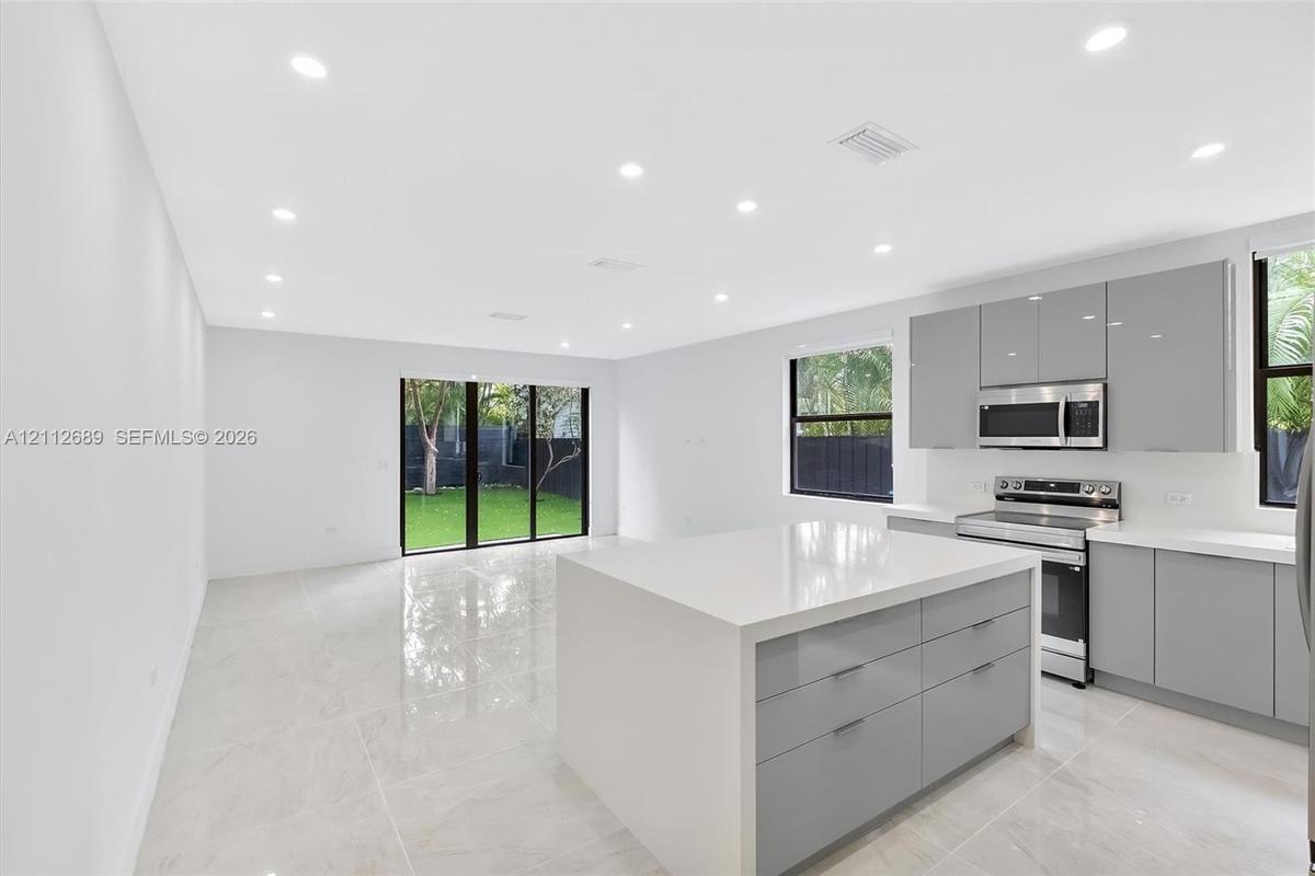 Open-concept kitchen featuring high-gloss cabinetry, a central island with a solid surface countertop, stainless steel appliances, recessed lighting, 